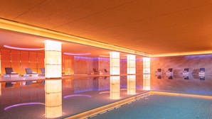 A modern indoor swimming pool with a long, narrow shape, surrounded by seating areas and illuminated pillars. - Rocase Hotel Wuxi (Wuxi)
