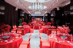 Un salón de banquetes con mesas redondas, manteles rojos y sillas a juego.