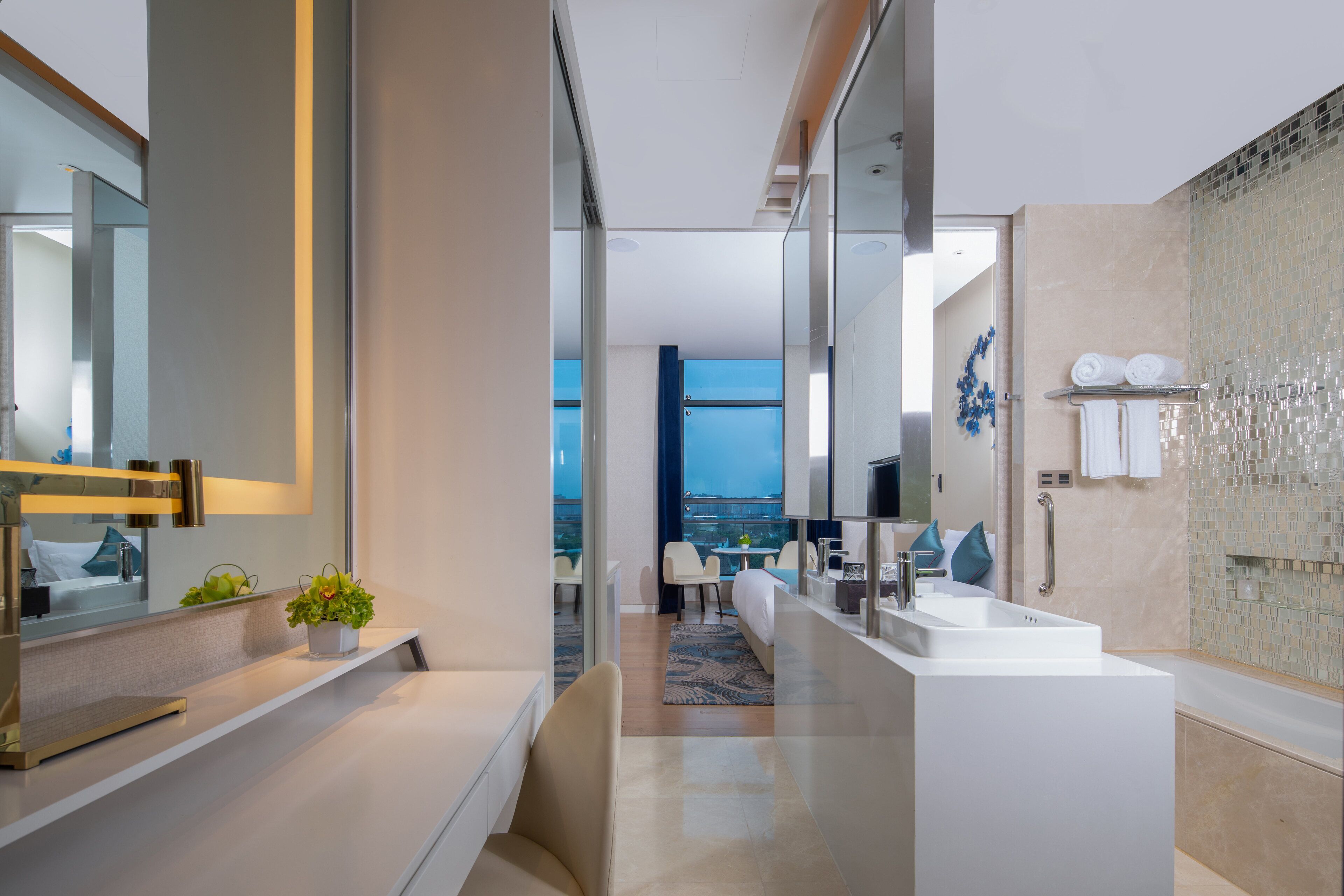 Une chambre d’hôtel moderne dotée d’un grand miroir, d’un lavabo blanc, d’une baignoire et offrant une vue sur la ville.