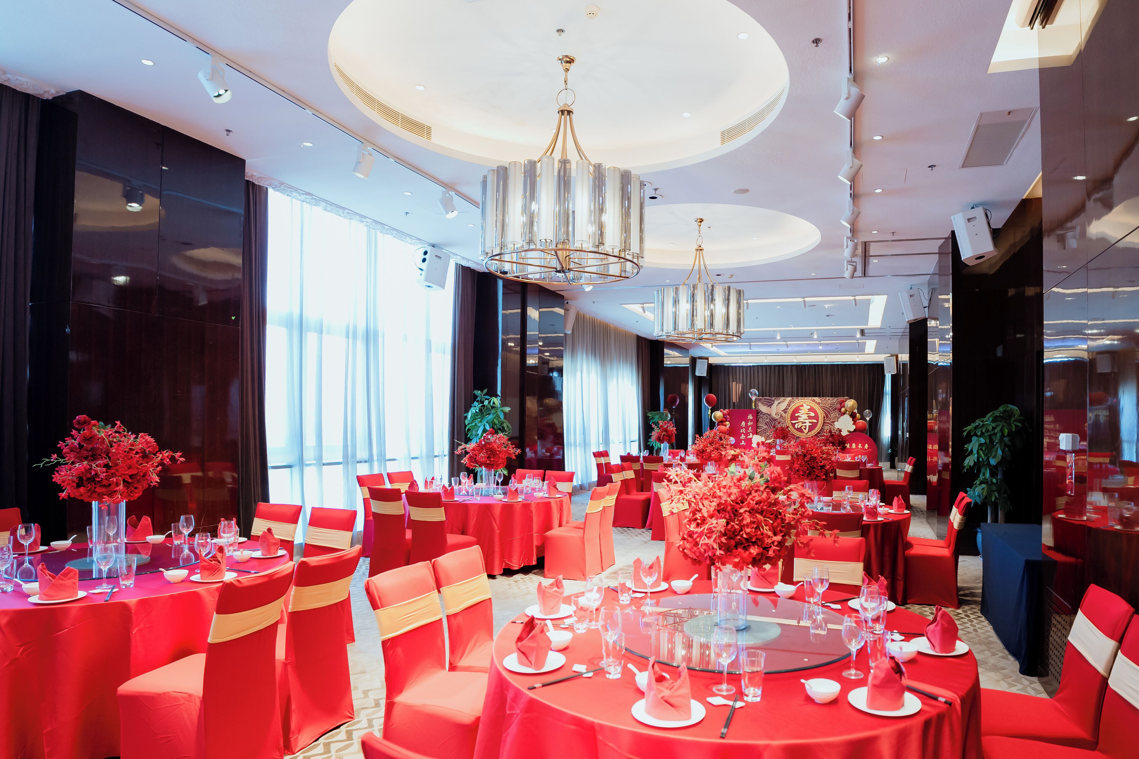 A spacious banquet hall with round tables, red tablecloths, and matching chairs.