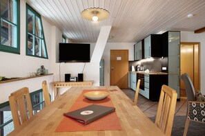 Un comedor con una mesa de madera, sillas, un televisor y una cocina al fondo.