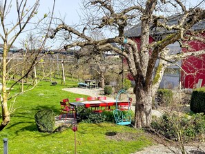 Un jardín con un columpio, sillas rojas y una mesa.