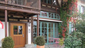 A building with a wooden balcony, a door with a heart-shaped decoration, and a window with green shutters.