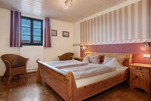 Un dormitorio con dos camas de madera, una silla de mimbre, una mesita de noche y una ventana con cortinas.