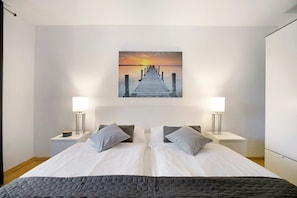 A hotel room with a bed, two bedside tables, a nightstand, a wall-mounted painting, and a night lamp. - Apartment 'Vicky' with Private Terrace, Balcony and Wi-Fi (Flensburg)