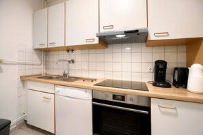 Una cocina con armarios blancos, lavavajillas, horno, cafetera y fregadero.