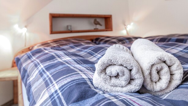 A bed with a plaid blanket and two rolled towels. - Apartment 'Nis Puk' with Private Terrace, Shared Garden and Wi-Fi (Rodenäs)