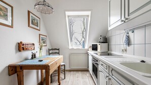 A kitchen with a window, a table with chairs, a microwave, and cabinets. - Apartment 'Nis Puk' with Private Terrace, Shared Garden and Wi-Fi (Rodenäs)