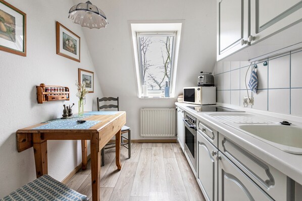 A kitchen with a window, a table with chairs, a microwave, and cabinets.