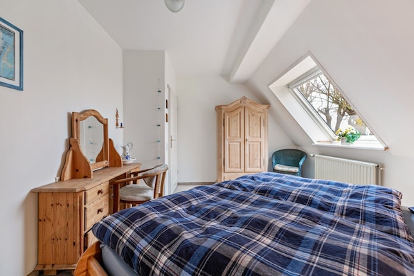 A bedroom with a bed, a dresser, a chair, a wardrobe, and a skylight.