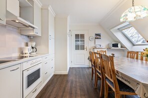 Una cocina con armarios blancos, una mesa de comedor de madera y vistas por un tragaluz.