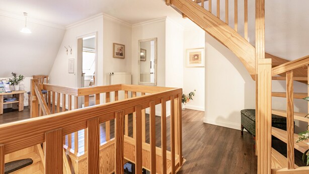 A wooden staircase with a railing, a dining area with a table and chairs, and a view of the living room. - Apartment 'Theodor Storm' with Private Terrace, Shared Garden and Wi-Fi (Rodenäs)