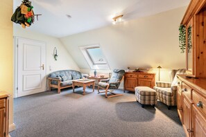 Un dormitorio estilo loft acogedor con techo inclinado, tragaluz, armario de madera, una mesita, un sofá y un sillón.