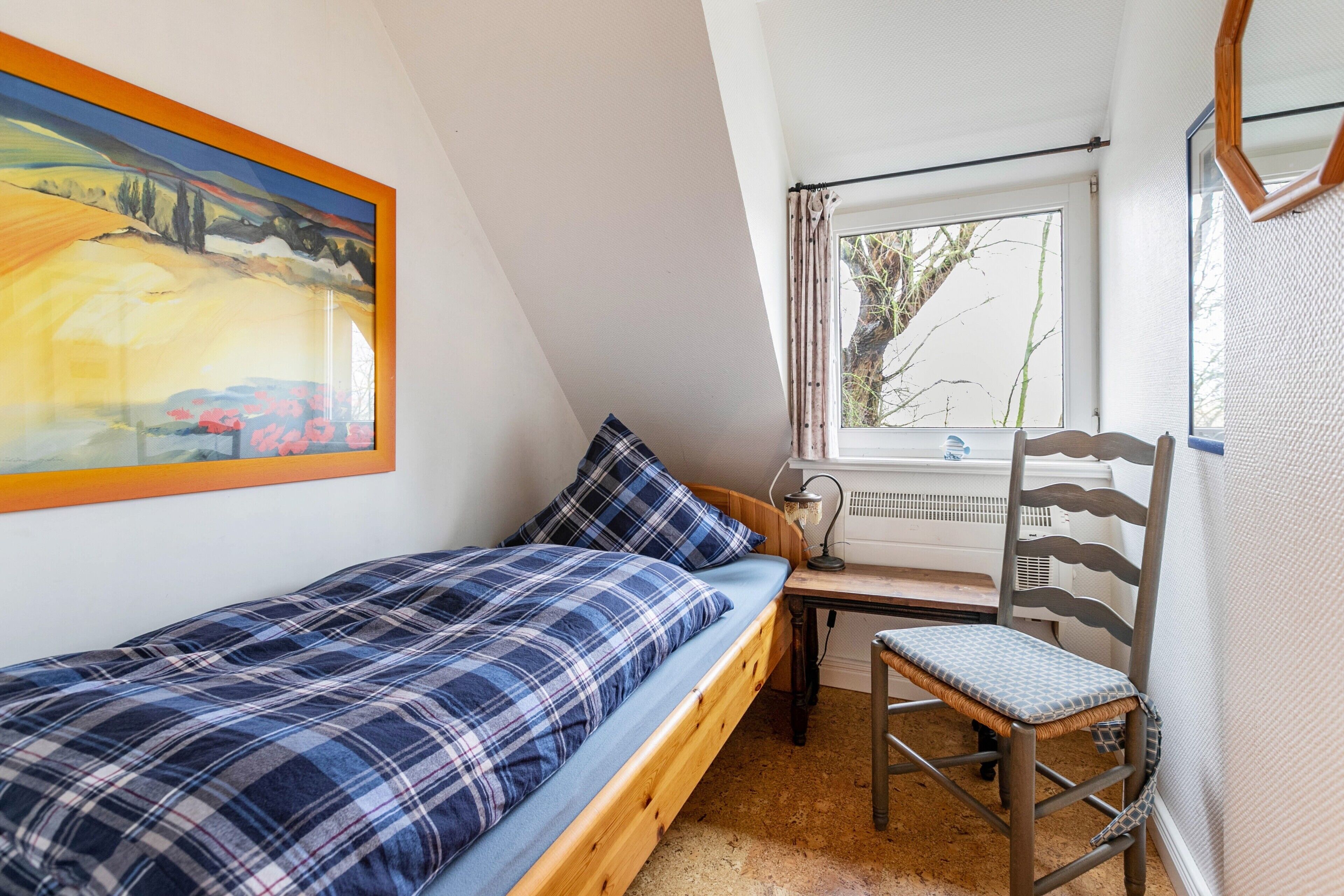 A small bedroom with a bed, a chair, a desk, and a window.