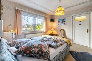 A bedroom with a large bed, a window with curtains, a lamp, a door, and a painting on the wall. - Apartment 'Erholung Pur' with Balcony and Wi-Fi (Hennstedt)