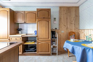 A compact kitchen with wooden cabinets, a dining table with a blue tablecloth, and a wooden dining chair. - Apartment 'Erholung Pur' with Balcony and Wi-Fi (Hennstedt)