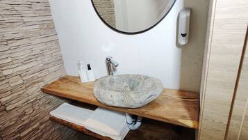 A bathroom with a stone sink, wooden vanity, and a stone wall.