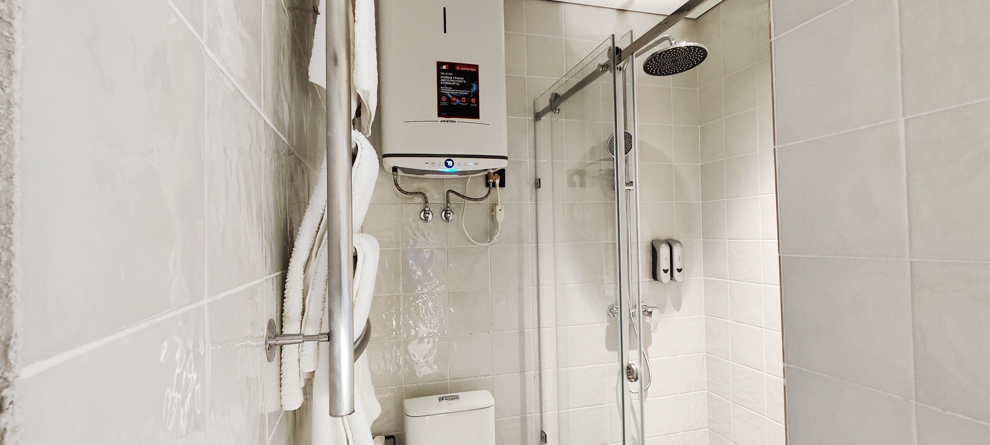 A modern bathroom with a glass-enclosed shower, a toilet, and a sink with a soap dispenser.