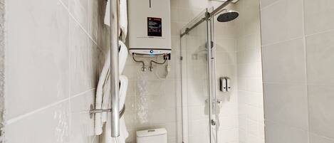 A modern bathroom with a glass-enclosed shower, a toilet, and a sink with a soap dispenser.