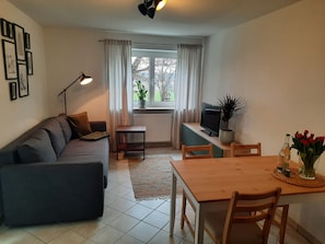 Un salon comprenant un canapé, une petite table, un téléviseur, une plante en pot et une table à manger avec des chaises.