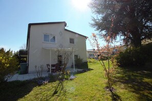 Une maison à deux étages avec une terrasse, un petit jardin et un arbre.