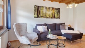 Ein Wohnzimmer mit einer Couch, einem Schaukelstuhl, einem Couchtisch und einem Gemälde eines Waldes.