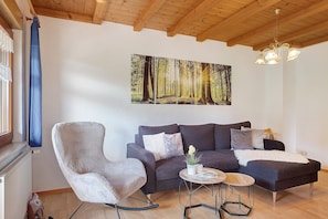 A living room with a sofa, a rocking chair, a coffee table, and a painting of a forest.