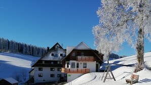Ein zweistöckiges Gebäude mit Balkon, einer Holzterrasse und einer Skiliftanlage in der Nähe.