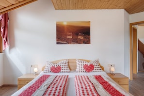 A bedroom with a bed, two bedside tables, a wall-mounted picture, and a wooden ceiling.