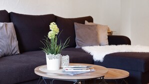 Ein Wohnzimmer mit einem dunkelgrauen Sofa, einem runden Holztisch und einer weißen Zierpflanze.