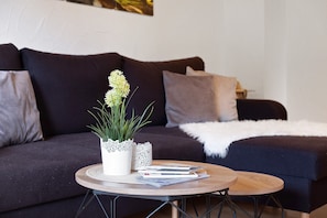 A living room with a dark-colored sofa, a round wooden coffee table, and a white decorative plant.