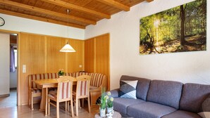 A room with a wooden ceiling, a dining table with chairs, a grey sofa, and a painting of a forest. - Holiday Apartment 'West' with Shared Terrace, Shared Garden and Balcony (Eisenbach (Hochschwarzwald))