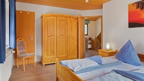 A bedroom with a wooden bed, a nightstand with a lamp, a wardrobe, and a chair. - Holiday Apartment 'West' with Shared Terrace, Shared Garden and Balcony (Eisenbach (Hochschwarzwald))