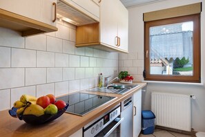 Une cuisine moderne dotée d’une cuisinière intégrée, d’une fenêtre offrant une belle vue et d’un panier de fruits posé sur le plan de travail.