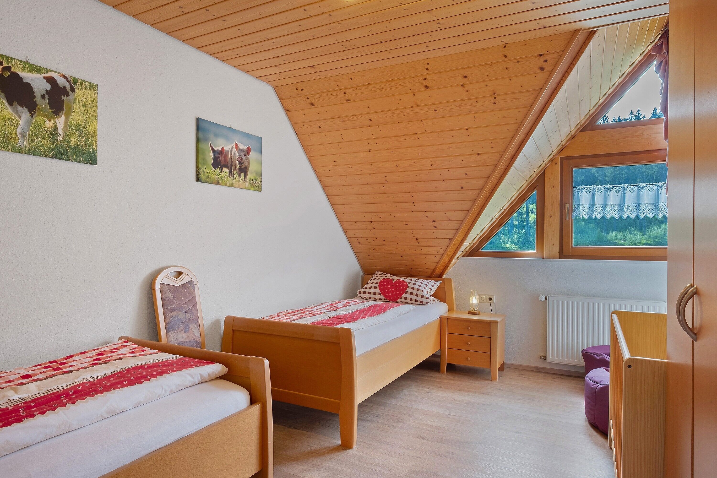 Ein Schlafzimmer mit zwei Holzbetten, einem Nachttisch, einer Kommode und einem Fenster mit Blick auf Grünflächen.