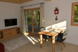 Uma sala de jantar com uma mesa de madeira, cadeiras, uma TV, um armário de madeira e uma janela grande com cortinas.