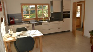 Een moderne keuken met een eethoek, houten kastjes, een raam met uitzicht en een deur naar een andere kamer.