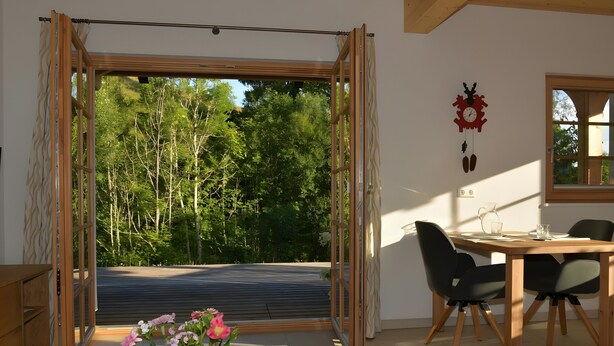 Een kamer met een schuifglasdeur naar een balkon, een eettafel met stoelen, een klok aan de muur en een kleine plant op de vloer.