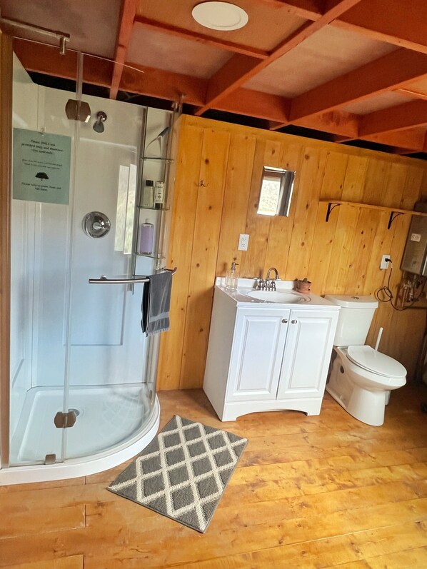 A bathroom with a glass shower, white sink, and toilet, wooden walls, and a small rug. - "Sweet Clover" - Yurts at Poncha Pass. A dark sky place to see the Milky-way. (Poncha Springs)