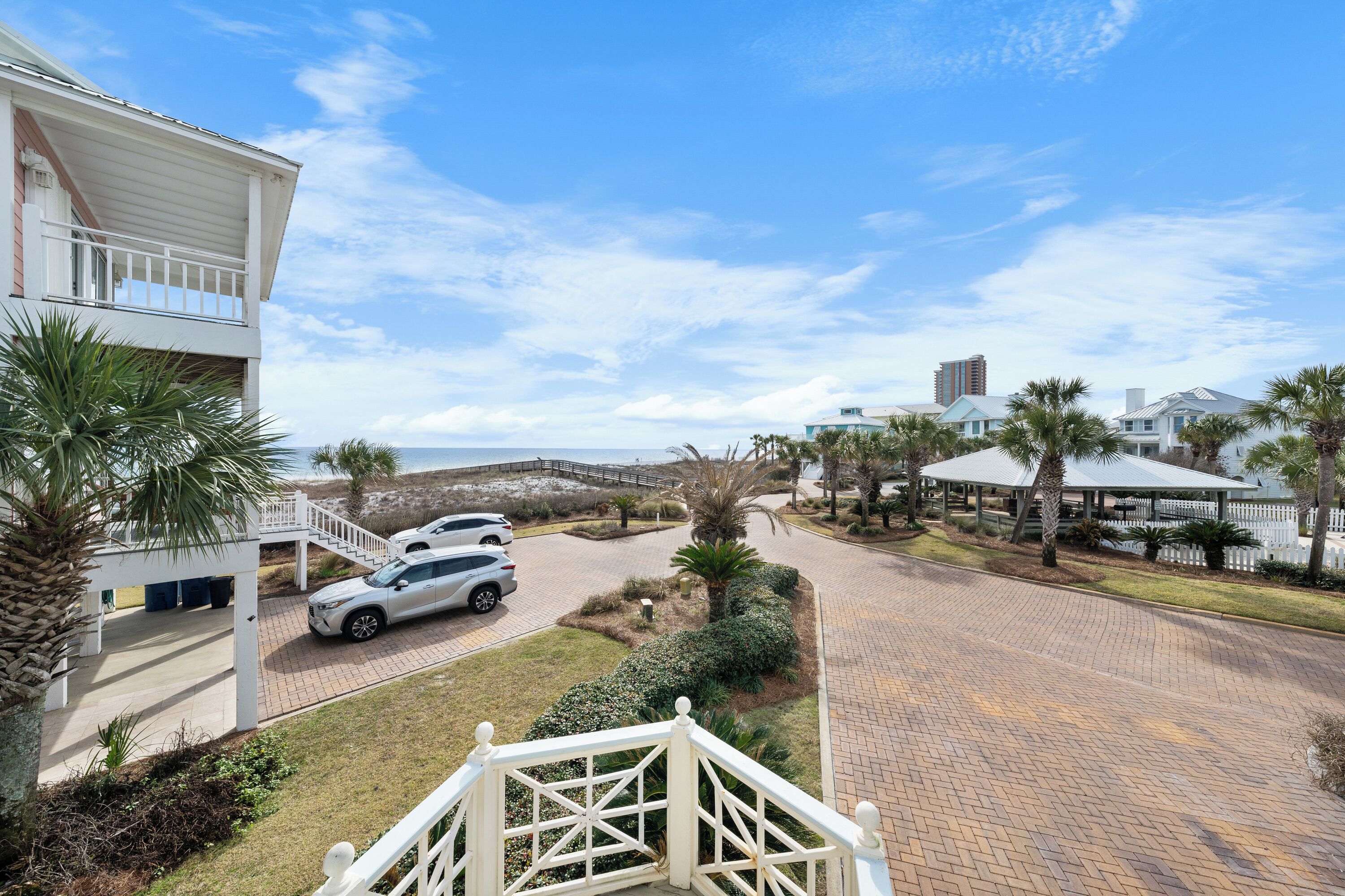 A gated residential area with a paved driveway, parked cars, and a white building with a balcony.