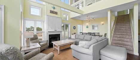 A spacious living room with a fireplace, a staircase, and a 'BEACH' sign on the wall.