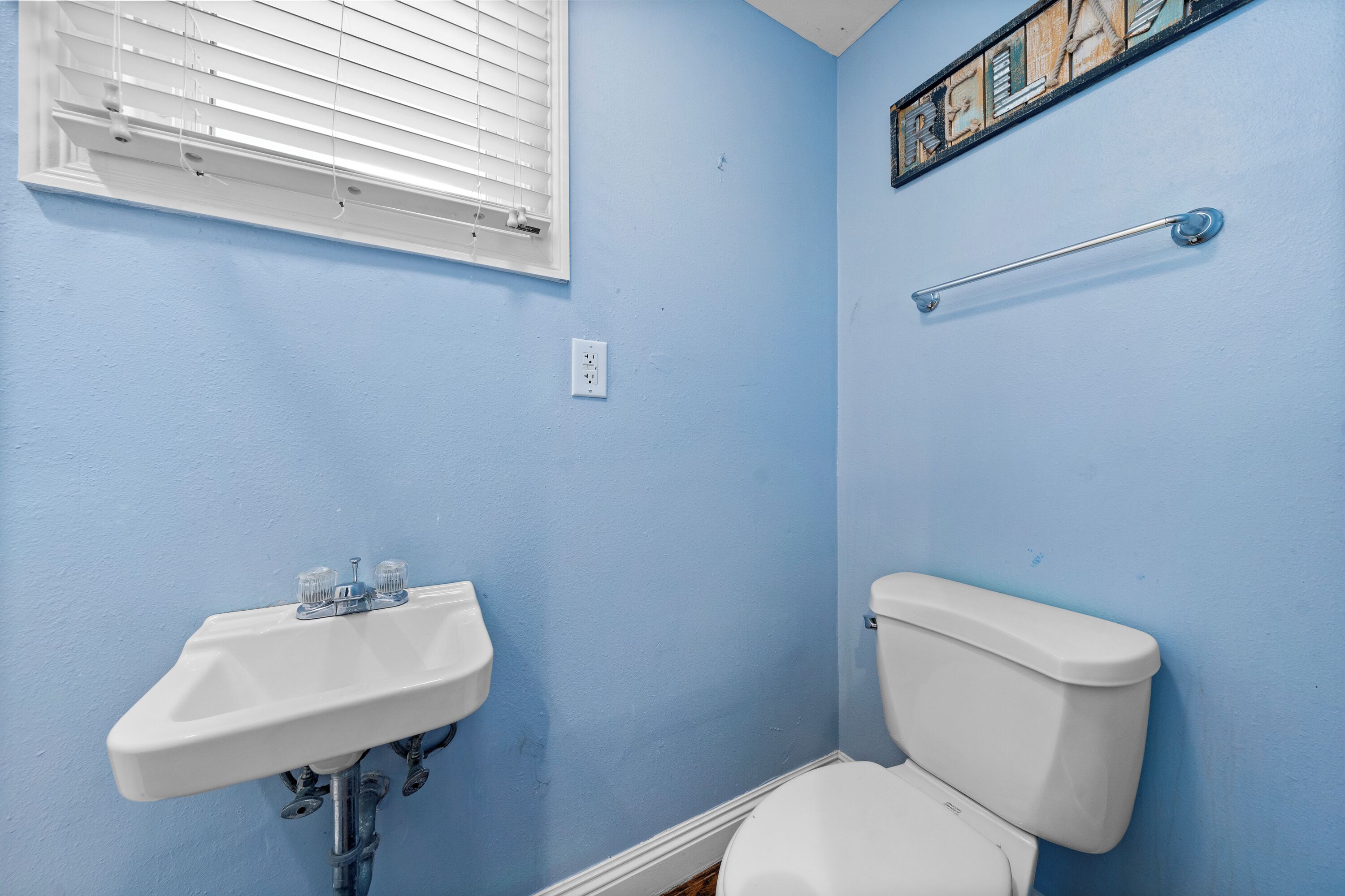 A bathroom with a white sink, toilet, and a window with blinds.
