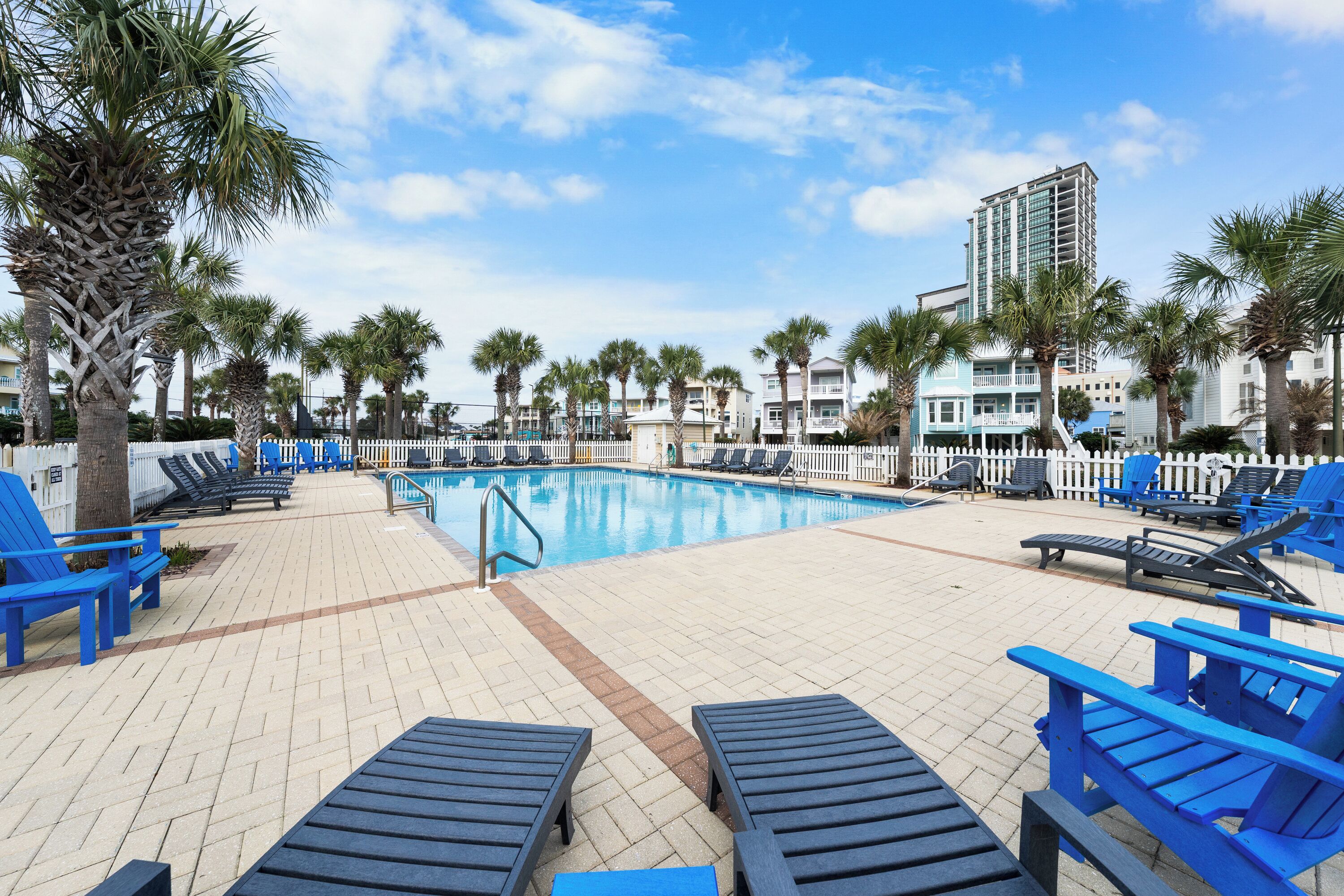 A poolside area with lounge chairs, palm trees, and a building in the background.
