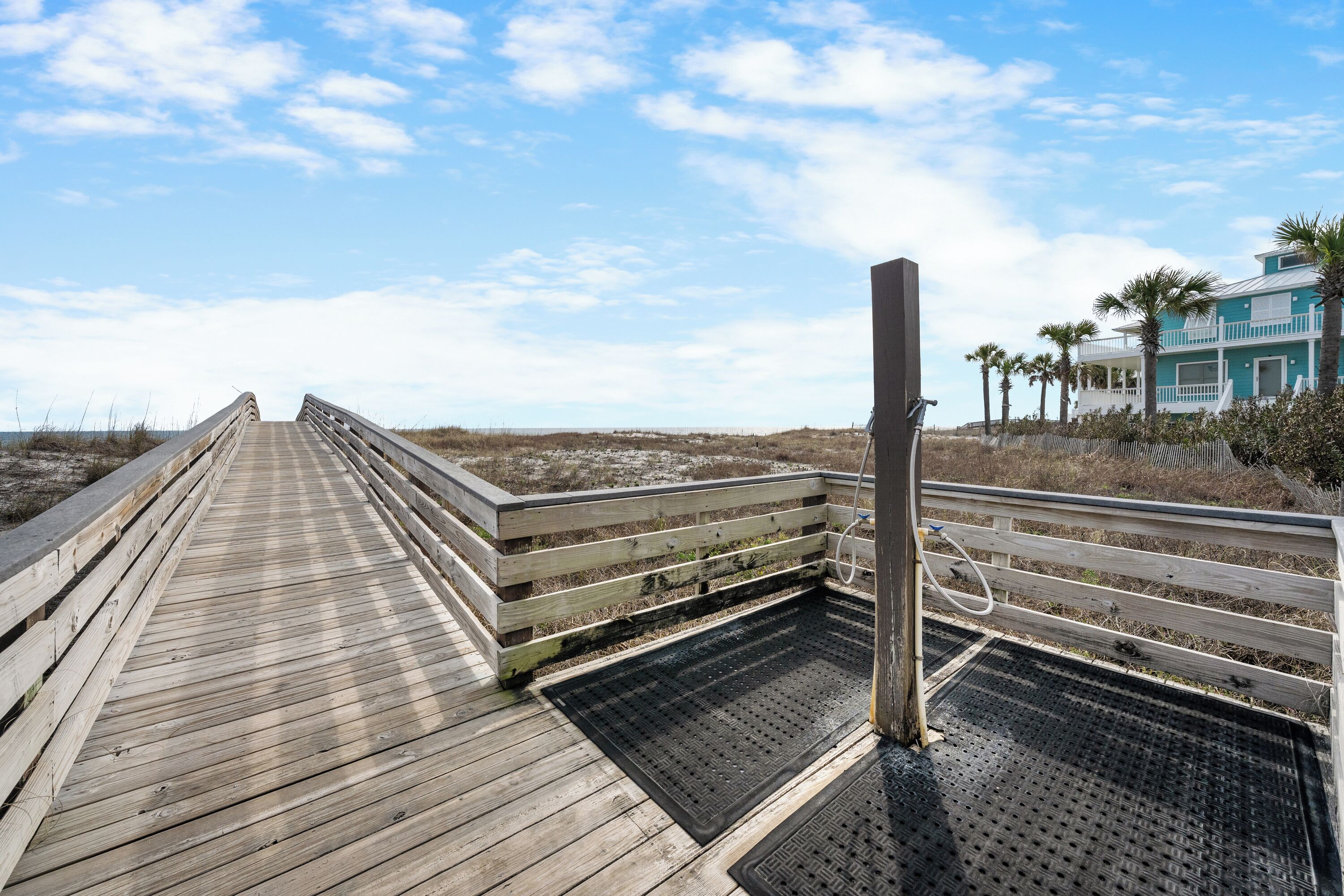 A wooden boardwalk leading to a beach area with a blue building and palm trees.