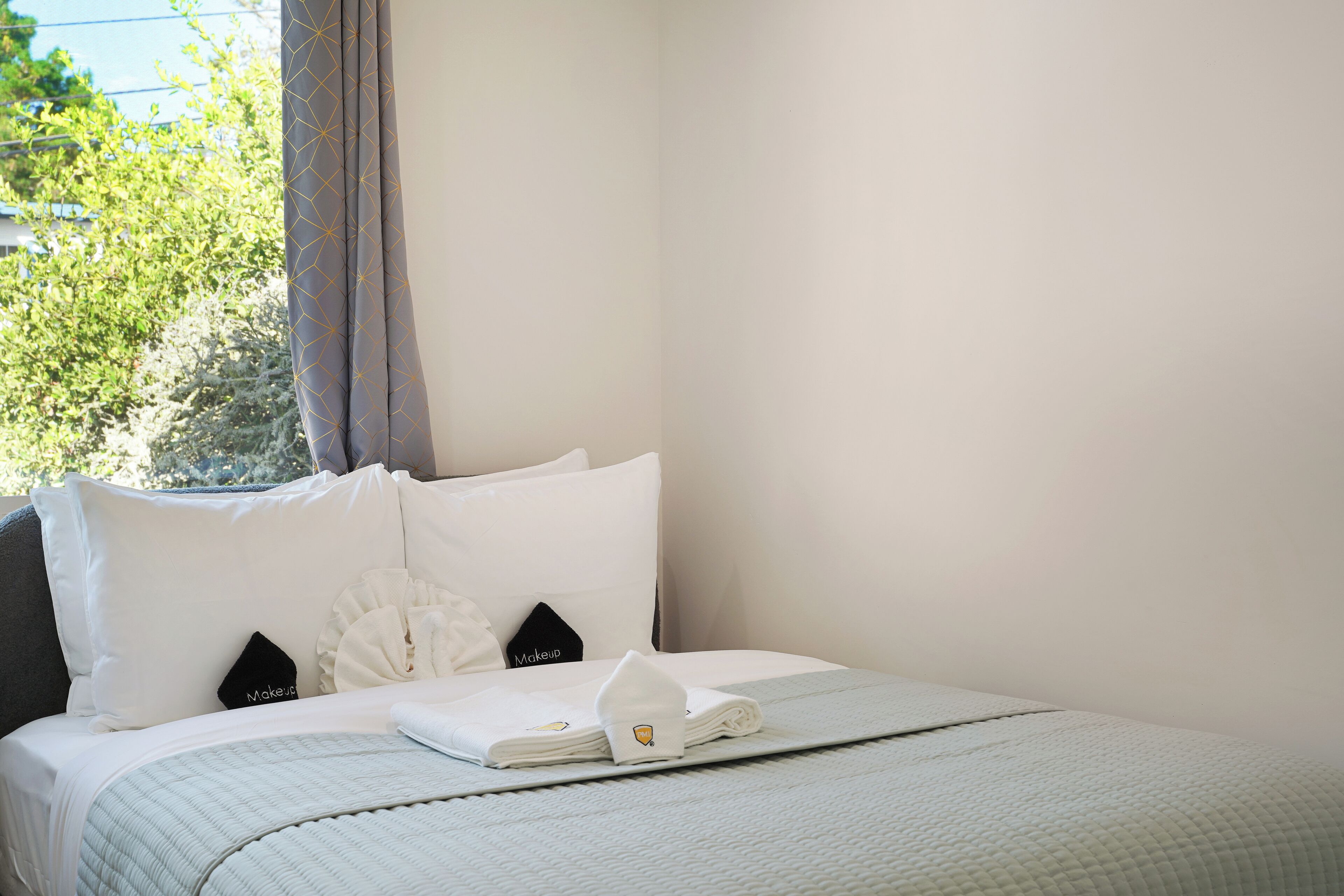 A neatly made bed with white bedding and pillows, a folded towel, and a small black pillow with "Makeup" written on it.