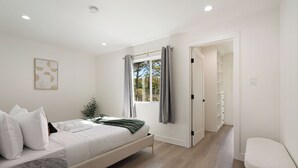 A bedroom with a bed, a bedside table, a chair, a window with curtains, and a door leading to a closet. - Oceanview Sunset View 3BR Luxe Home Yard (Pacifica)