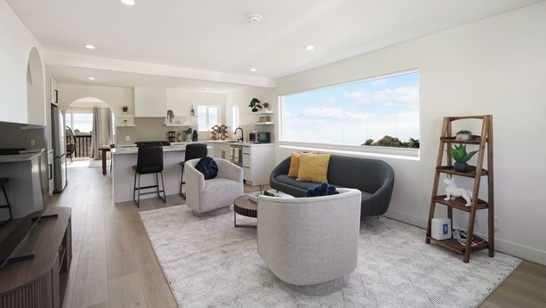 A modern living room with a grey sofa, a white armchair, and a grey ottoman. There is a wooden shelf with a plant and a white statue. A large window provides a view of the sky. - Oceanview Sunset View 3BR Luxe Home Yard (Pacifica)