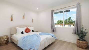 A bedroom with a bed, a window with curtains, a potted plant, and a wall-mounted plant.