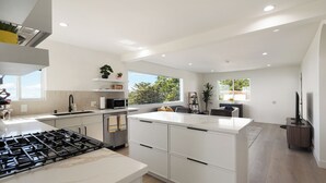 A modern kitchen with white cabinetry, a central island, and a gas stove. - Oceanview Sunset View 3BR Luxe Home Yard (Pacifica)