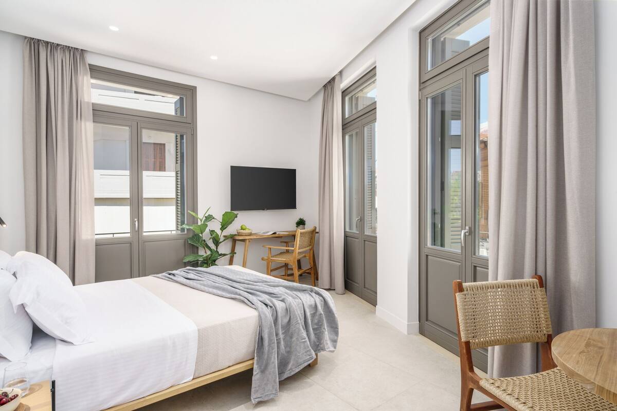 A modern bedroom with a bed, a desk, a chair, and a TV.